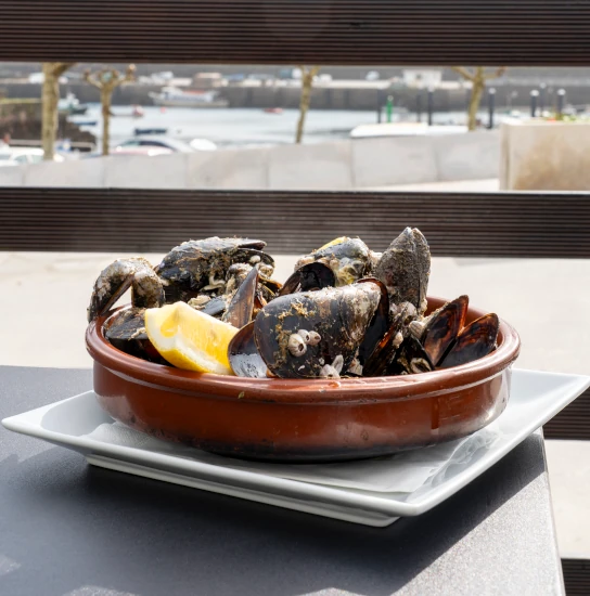 Cazuela de mejillones con limón en una mesa de A Cantina Fisterra con vistas al puerto